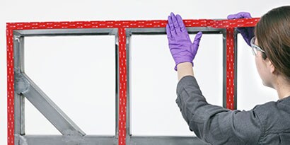 Pracovník připevňuje pásku VHB k rámu za účelem následného připevnění k panelu
