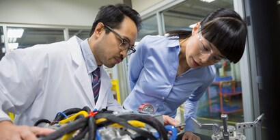 Průmyslová komunita společnosti 3M Obrázek dvou techniků zkoumajících v laboratoři robotické díly.

