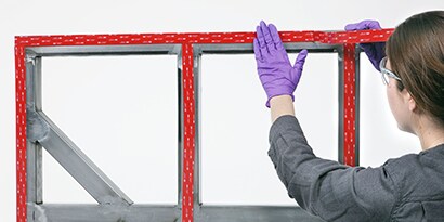 Technik aplikuje průmyslovou lepicí pásku při lepení panelu k rámu
