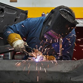 Technik v továrně svařuje kovové podklady a kolem létají jiskry